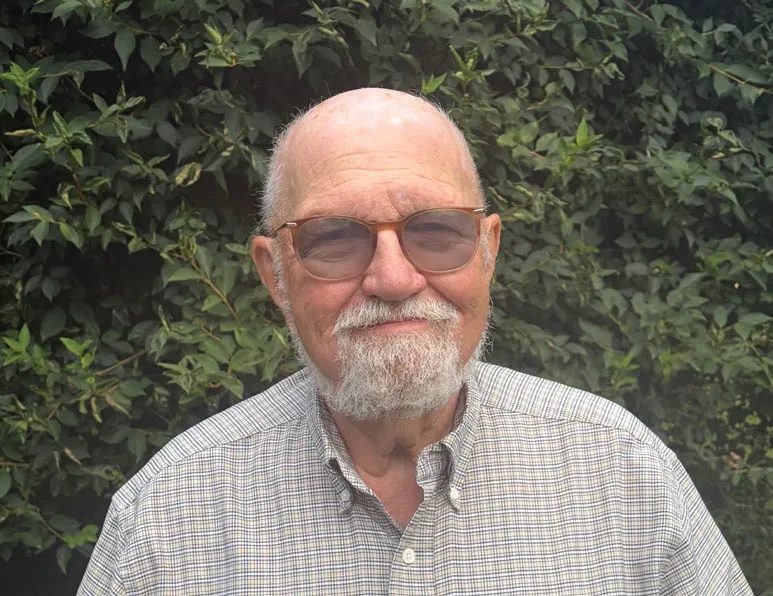 Jim Bednar, smiling outdoors in a checked shirt in front of a green hedge